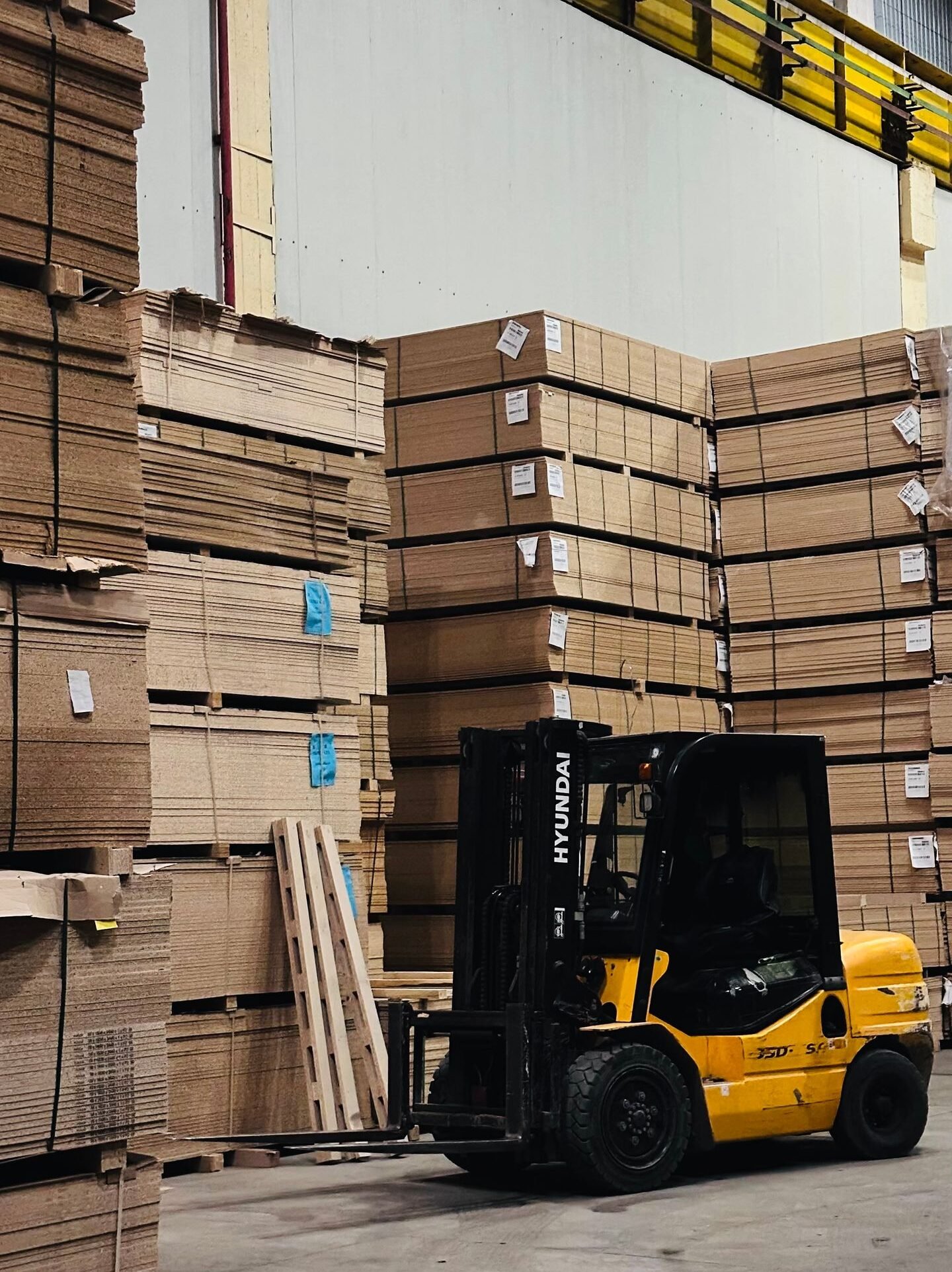 A yellow forklift organizes large stacks of cardboard boxes in a spacious warehouse.
